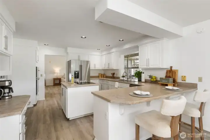 Bright upgraded kitchen with white cabinetry, generous counter space, bar seating, and a new stainless steel refrigerator—designed for everyday comfort and elegant entertaining.