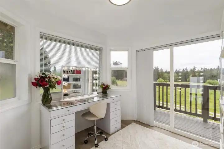 Inside the primary bedroom, a bright private sitting or vanity area opens to the deck, capturing peaceful acreage views and natural light—an elegant retreat within the main-level suite.