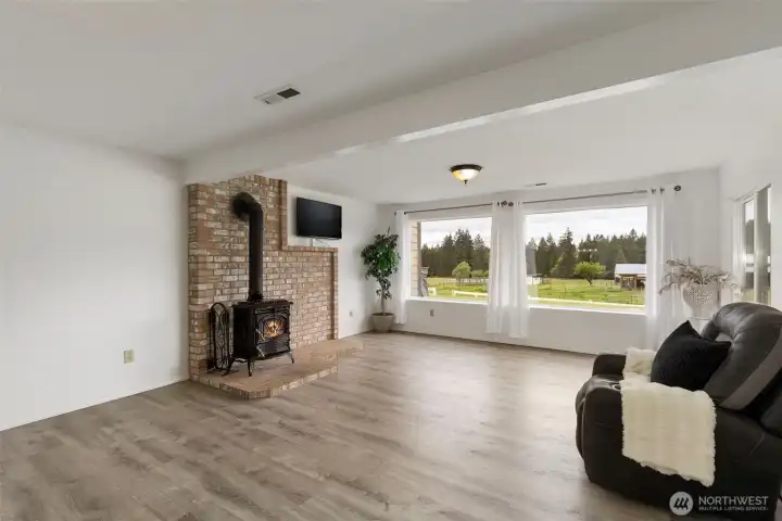 Downstairs family room filled with natural light, featuring a cozy wood stove, expansive windows, and peaceful acreage views—an inviting space for relaxing, gathering, and flexible everyday living.