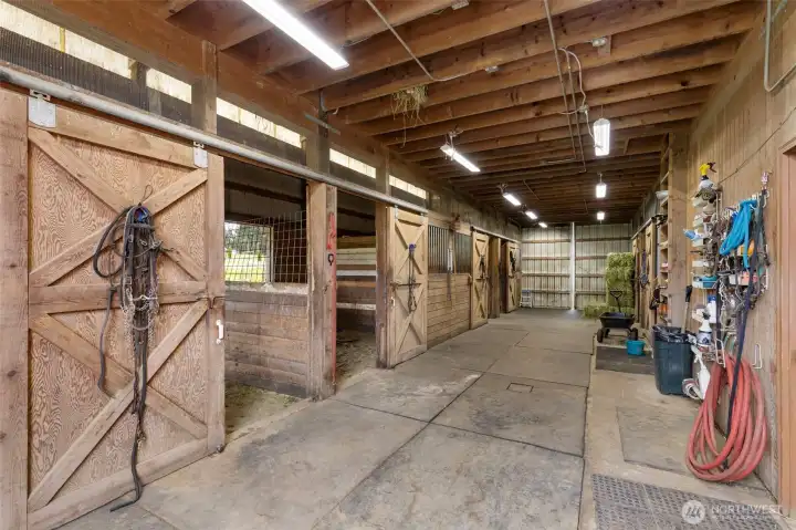 Well-equipped 4-stall horse barn with wide aisle, tack storage, lighting, wash area, and functional workspace—designed for efficient daily care and elevated equestrian living.