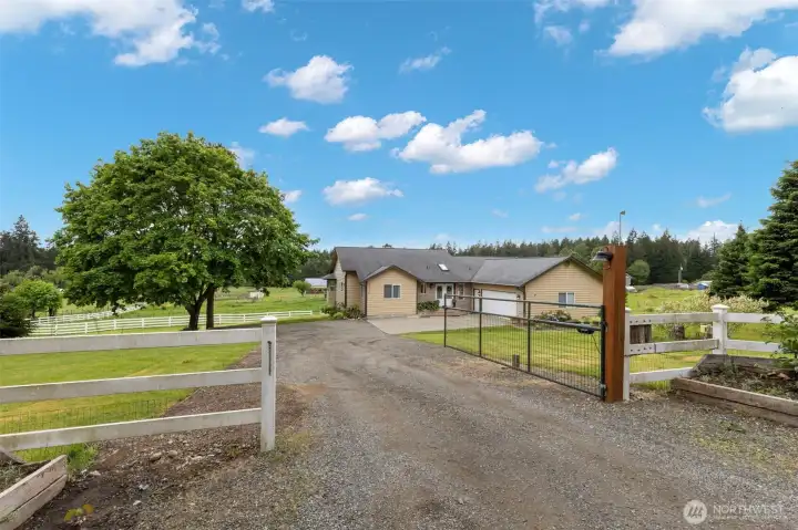 Main gated entrance to a luxury Port Orchard acreage home, framed by white fencing, open pastures, mature trees, and a private driveway.