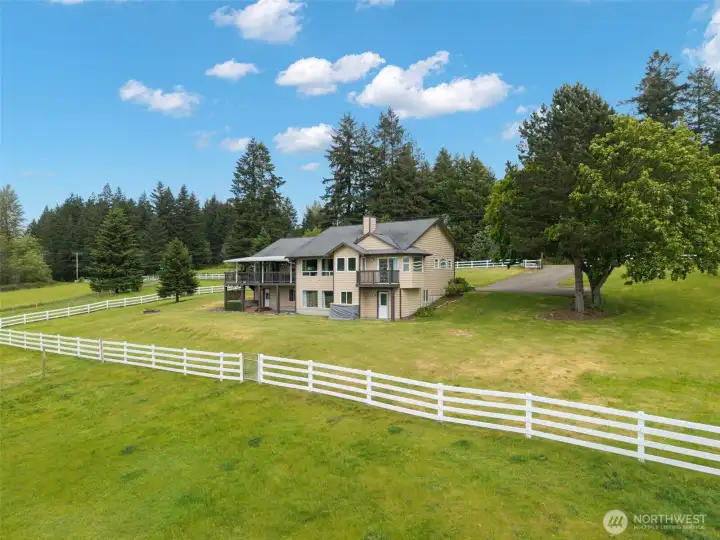 Rear view of the home showcases the new white fence behind the house, adding classic curb appeal, defined outdoor space, and a polished finish to the private acreage setting.