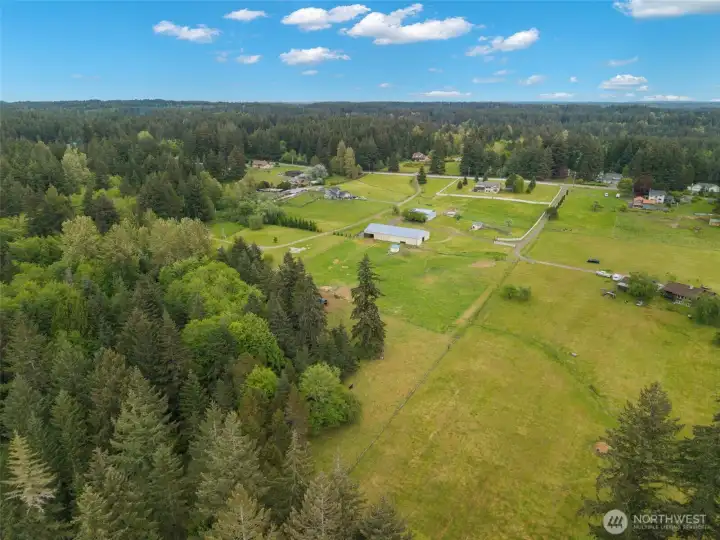 Rear aerial view showcasing expansive acreage, open pastures, mature evergreens, and equestrian outbuildings—capturing the privacy, scale, and natural beauty of this Port Orchard estate.