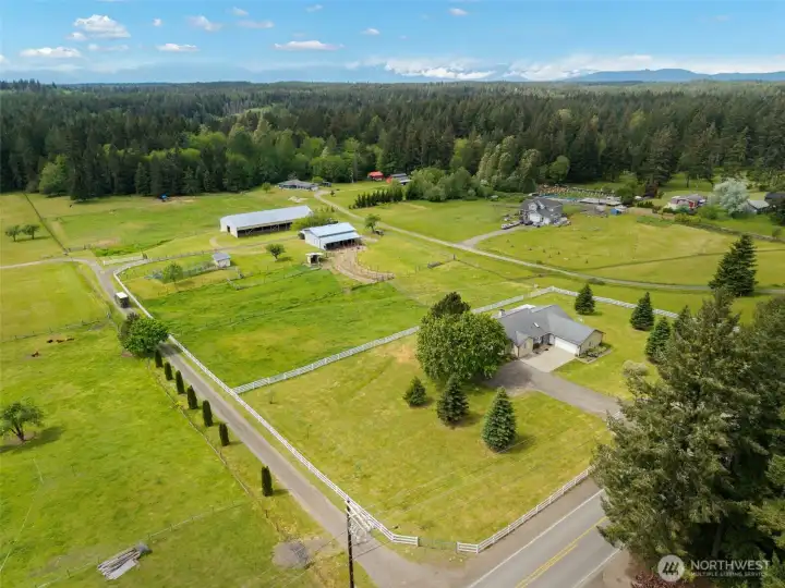 Aerial view of this luxury acreage property showcases the new white fence behind the home, defining the grounds with classic charm, privacy, and polished equestrian appeal.