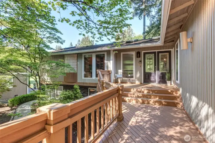 Inviting front entry with a spacious deck, surrounded by lush greenery and a peaceful wooded setting.