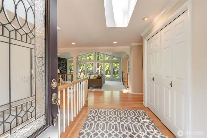 Bright, welcoming entry with skylight overhead, hardwood flooring, and an open sightline into the sunlit living spaces beyond.