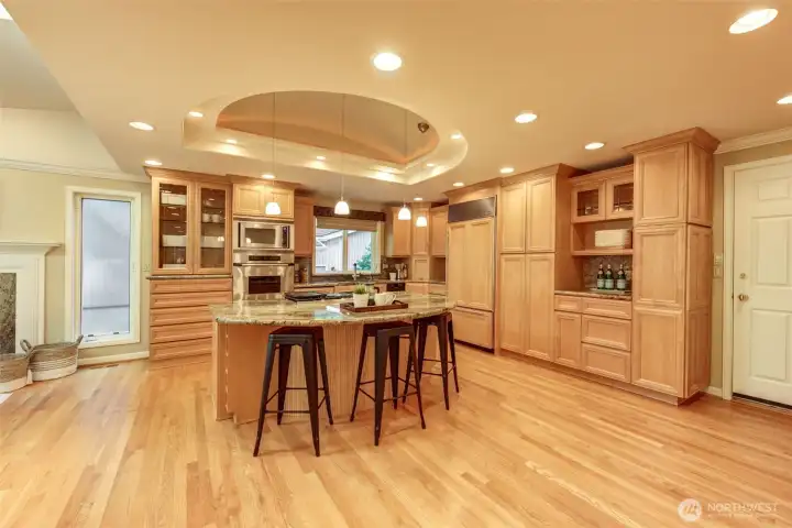 Extensively remodeled kitchen featuring granite countertops, abundant maple cabinetry, oven with warming drawer, built-in microwave, cooktop with telescopic vent, fridge with pull-out freezer drawer beneath, integrated toaster, coffee bar area, illuminated display cabinetry, under-cabinet lighting, recessed lighting, pendant lighting, and a large island with seating.