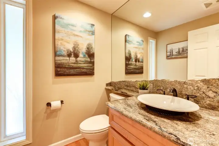 Stylish powder bath off the kitchen with rich granite countertops and a unique full-height granite backsplash that continues seamlessly onto the mirror surround.