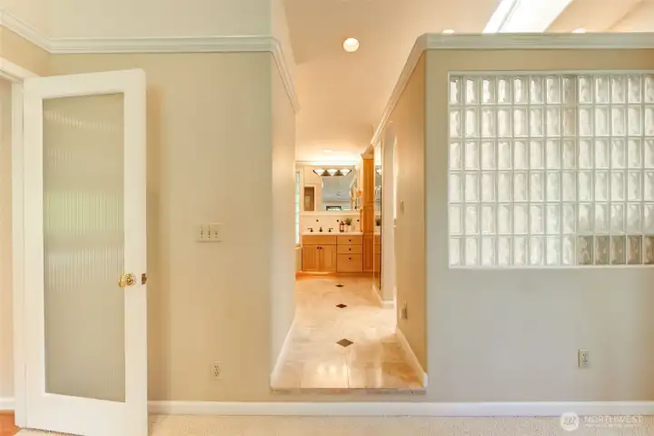 Private primary bath entrance accented by glass block detailing and a spacious en-suite layout beyond.