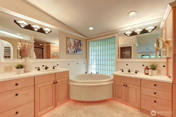 Spa-inspired primary bath with dual vanities, soaking tub, generous storage, and a glass block feature window wall that fills the space with soft natural light.