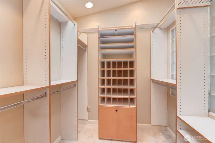 Spacious walk-in closet with extensive custom organization, adjustable shelving, and dedicated accessory storage throughout. This area stays bright with the skylight above, as well as light peeking through the glass block wall.
