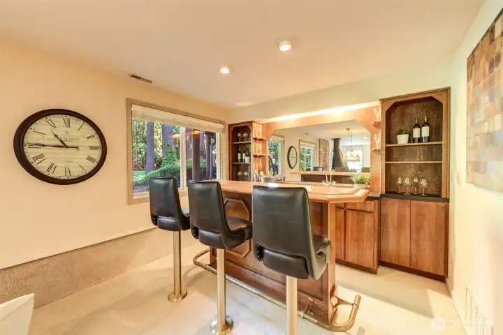 Classic wet bar with seating, mirrored accents, built-in shelving, and a cozy lounge atmosphere.