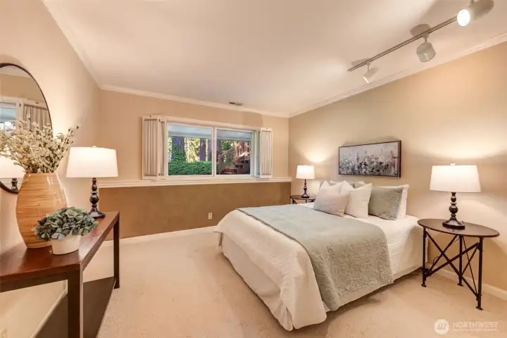 Comfortable lower-level bedroom with soft natural light, backyard views, and a quiet retreat feel. Track lighting and built in shutters. Large closet not pictured.
