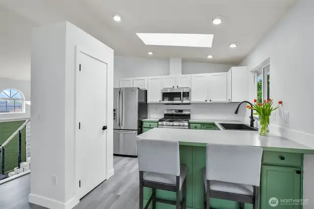 Updated kitchen with white shaker cabinets, green base cabinets, stainless steel appliances, and skylight for natural light.