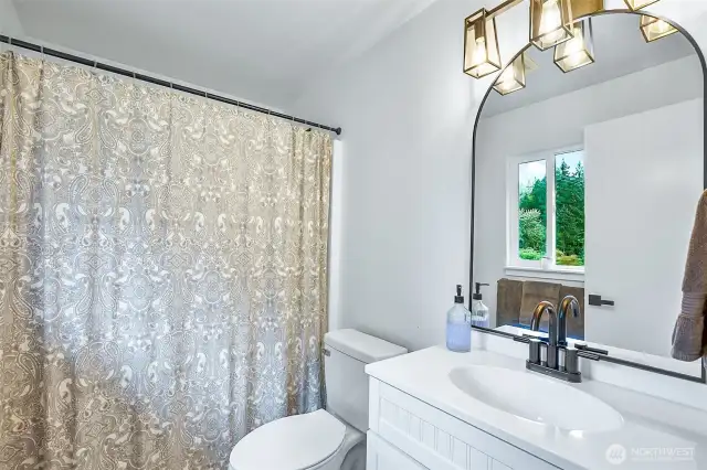 Updated full bathroom with modern lighting, large framed mirror, and window for natural light.