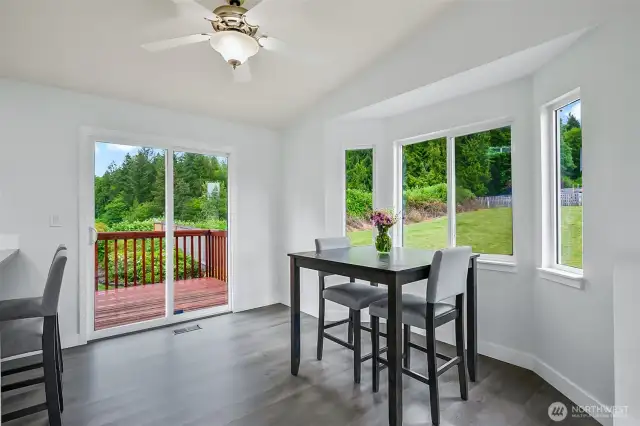 Dining area with vaulted ceiling, large bay-style windows, and sliding door leading to the back deck and yard.