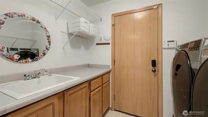 Main level unity room features new washer and dryer, a large sink, cabinets for storage, and entrance from the garage