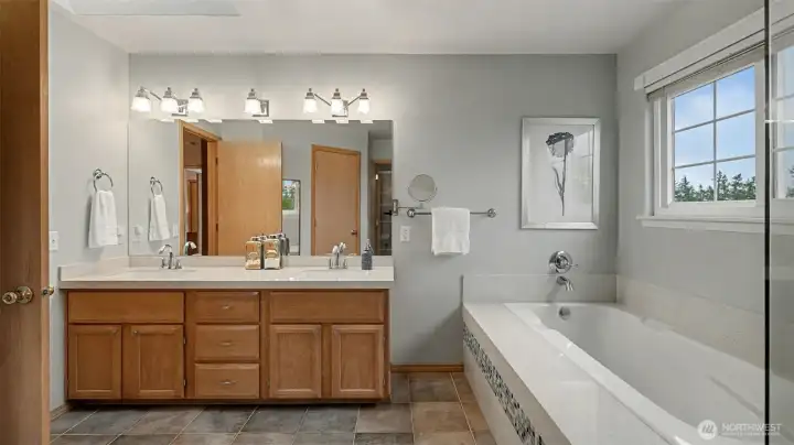 Dual sinks and luxurious soaking tub in this spa-inspired primary bathroom (walk-in closet to the left)