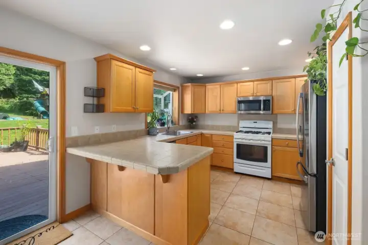Functional kitchen layout with extensive cabinetry, wraparound tile countertops, recessed lighting, and access to the backyard deck.