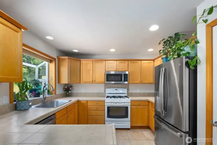 Bright kitchen with natural wood cabinetry, stainless refrigerator, gas range, and windows overlooking the property.