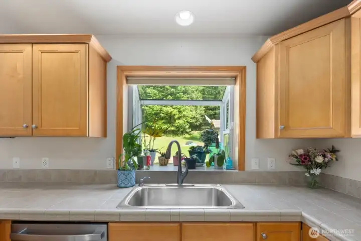 Kitchen sink positioned beneath a large picture window overlooking the backyard and surrounding greenery.
