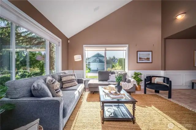 Step inside to the elegant formal living room flooded with natural light. It features vaulted ceilings, detailed wainscoting, large picture windows, and soothing paint tones.