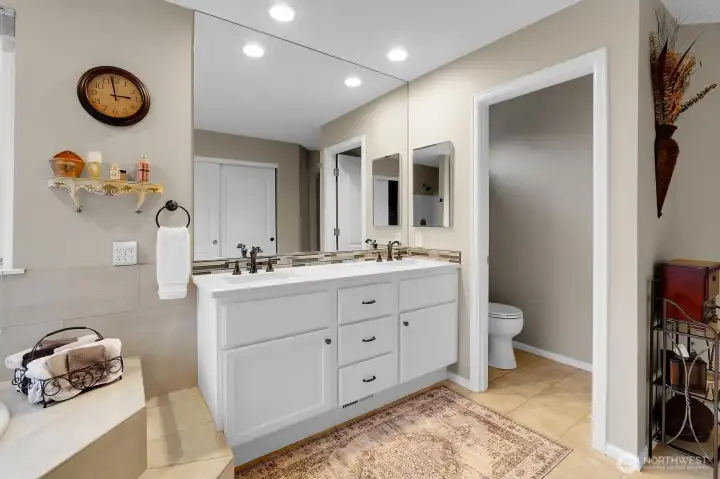 Primary suite bathroom with walk in shower, tub, walk in closet, double vanity, and quartz counters