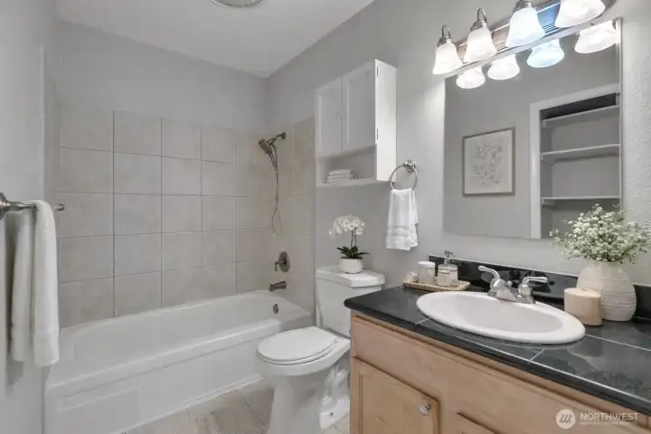 This clean and bright bathroom features a full tub and shower, a spacious vanity with ample counter space, and modern lighting, creating a fresh and functional space.