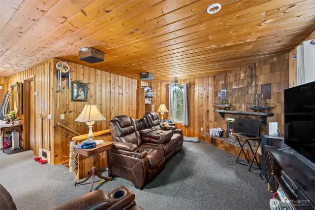 Main level living room with wood fireplace, built-in desk, and knotty pine walls and ceiling.