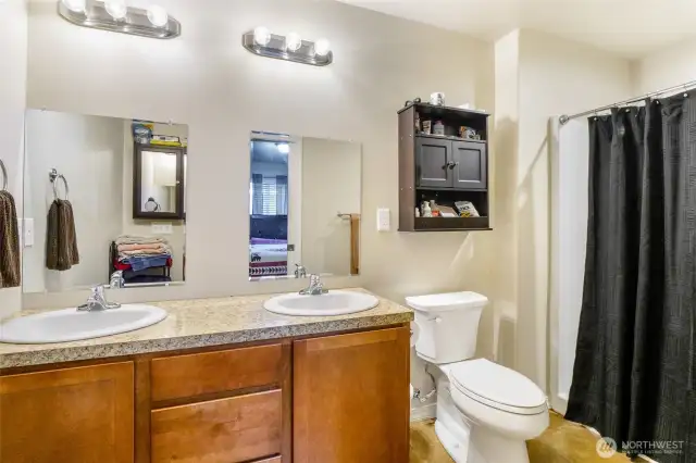 Dual-sink primary bathroom with walk-in shower with plenty of cupboard space, and an additional cupboard on the wall to hold personal effects.
