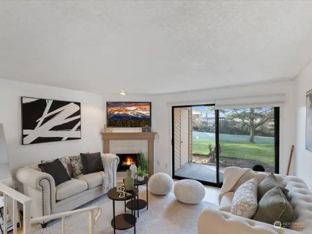 Spacious living room with wood burning fireplace, open view of the grounds and doors to the covered patio.