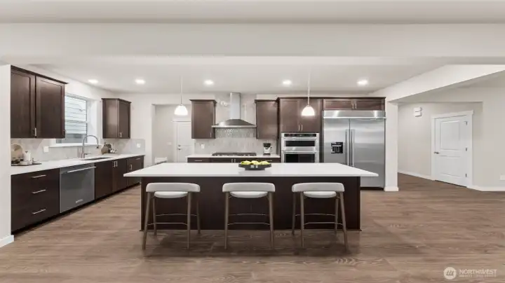 Large quartz center island to gather around.  Gourmet kitchen with large center island, quartz counters, loads of cabinets, built-in 48" fridge and in-wall oven & microwave next to your large family room. Actual home is under construction and materials, colors, and finishes will vary. See site agent for details.