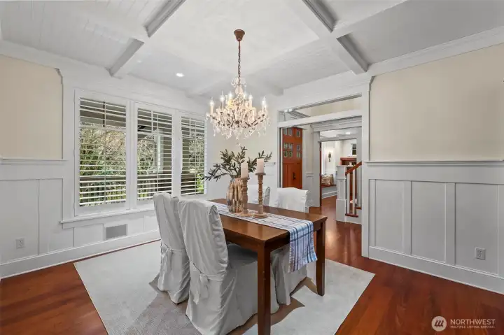 An inviting dining room with a crystal chandelier, coffered ceilings and wainscotting