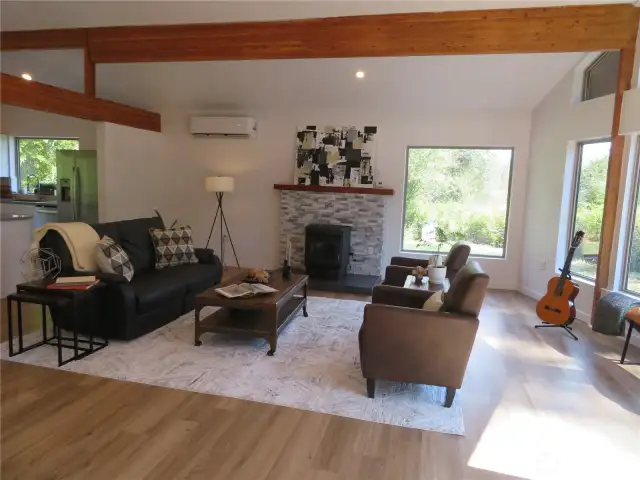 Living room with vaulted ceilings and wooden beams throughout this area including kitchen and dining area. Pellet stove shown here.