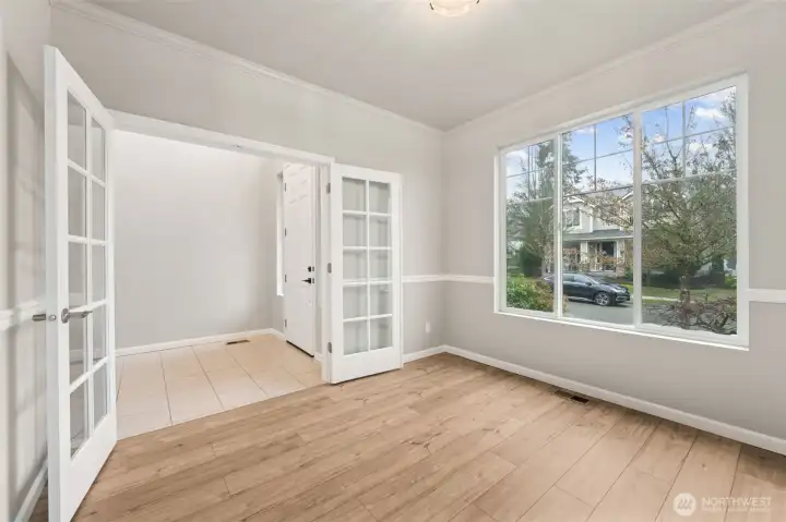 This den understands first impressions. Full glass French doors give it that classic, grown-up feel, while the chair rail adds just enough detail to make the walls feel finished. Soft dove gray paint keeps things calm and current, and the wide plank laminate flooring brings in warm, medium wood tones that ground the space. The oversized picture window steals the show, with those upper accent panes adding architectural interest without going fussy. Office, library, or stylish flex room, this space knows how to multitask.