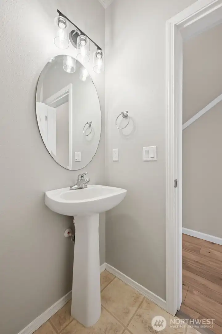 This powder room is compact but thoughtfully styled. The pedestal sink keeps it feeling uncluttered, while the beveled round mirror and modern overhead lighting add personality. Tile flooring stands up to traffic with ease, and the location just off the entry hall makes it convenient without being intrusive. It’s a quick stop that still feels considered, which is exactly how a powder room should work.