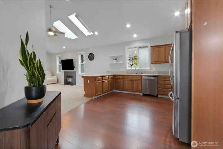 This beautifully connected kitchen and living area blends functionality with comfort, featuring generous prep space, stainless appliances, and rich cabinetry. Natural light from skylights above and large windows beyond fills the space, while the open sightlines to the family room invite effortless hosting and relaxed evenings at home.