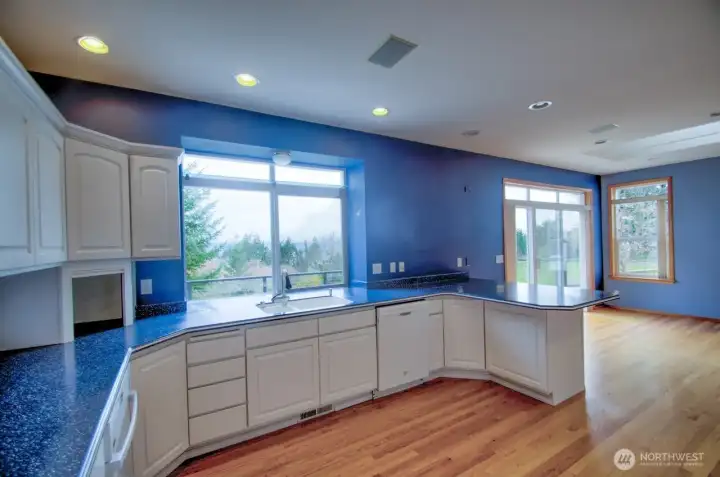 Oriented towards the view, well planned kitchen with white cabinetry, granite countertops, breakfast nook, double oven, appliance garage, and gleaming wood floors.