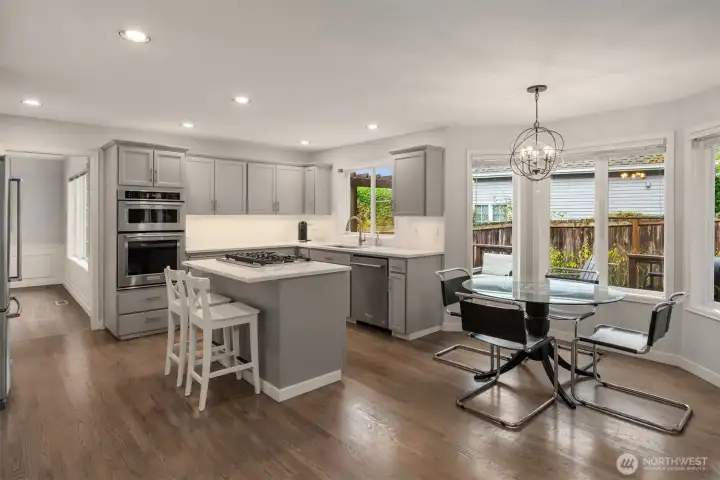 Recently updated kitchen features slab quartz countertops, stainless appliances including gas range, island with seating, upgraded lighting and niche with bay windows looking out to backyard.