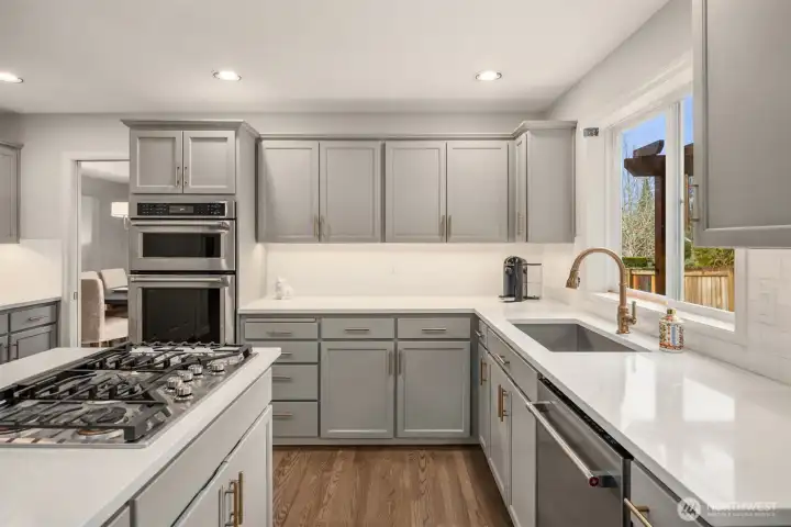 Kitchen features under-cabinet lighting, island with gas range plus down draft, slab quartz counters with under-mount stainless trough sink.
