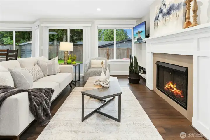 Cozy yet elegant living space with custom fireplace mantle, oversized windows, and peaceful backyard views creating the perfect atmosphere for relaxing or entertaining.