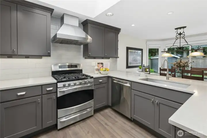 Gourmet kitchen with GE Profile dual-fuel range, commercial-grade vent hood, subway tile backsplash, quartz counters, and Kohler fixtures.