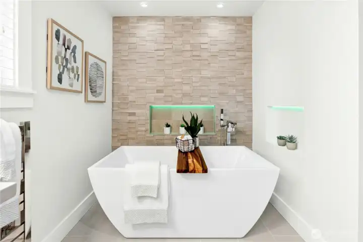 Modern freestanding soaking tub with elegant stone accent wall, built-in illuminated niche, and calming spa-like design creates the perfect luxury retreat experience.