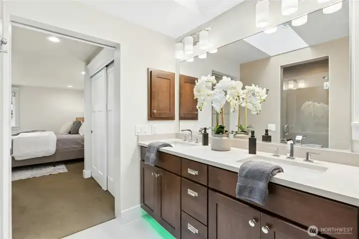 Bright and modern primary bathroom with expansive dual-sink vanity, sleek contemporary fixtures, skylight, and seamless connection to the walk-in shower and soaking tub area.
