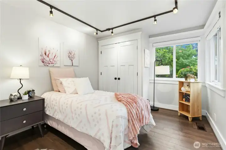 Comfortable and inviting secondary bedroom with large windows, rich hardwood flooring, custom closet doors, and abundant natural light.