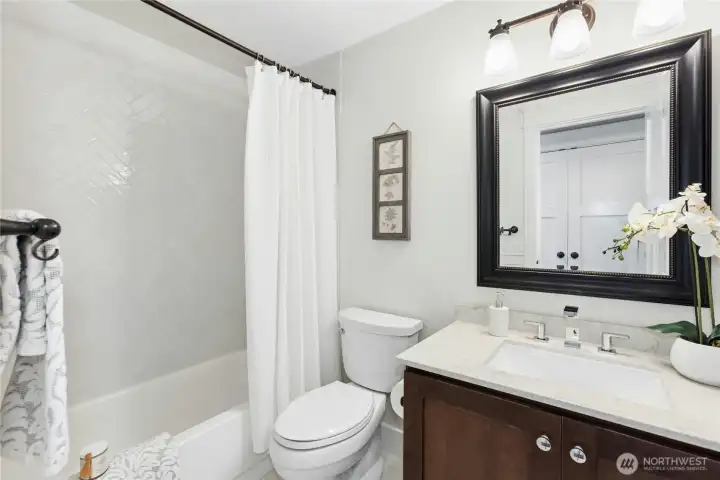 Stylishly updated guest bathroom featuring quartz counters, modern fixtures, designer mirror, and timeless white tile shower surround.