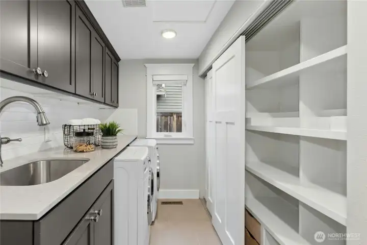 Well-designed utility room with extensive cabinetry, quartz counters, utility sink, and oversized custom shelving for exceptional storage and organization.