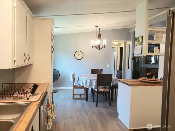 An Opposite Picture of the Dining Room and Kitchen from the Front Entry Door Showing Newer Painted Interior, White Trim, and Vinyl Plank Flooring Looking from the Utility Room