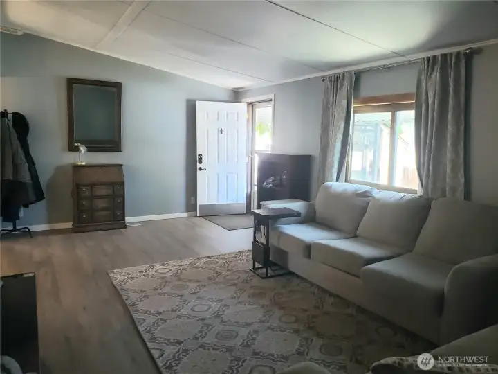 An opposite View of the Huge Living Room Looking into the Living Room and the Open Front Entry Door Showing New Interior Paint, White Painted Trim and Vinyl Plank Flooring.