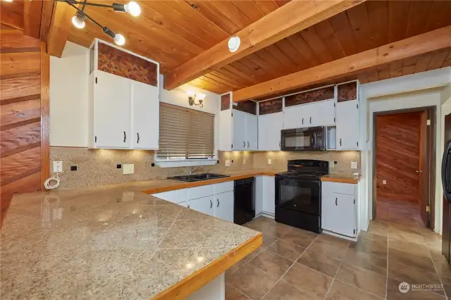 This kitchen has large tile countertops and accent lighting in the panels above and cove lighting below the cabinets. The lighting and countertops really brighten up the space.